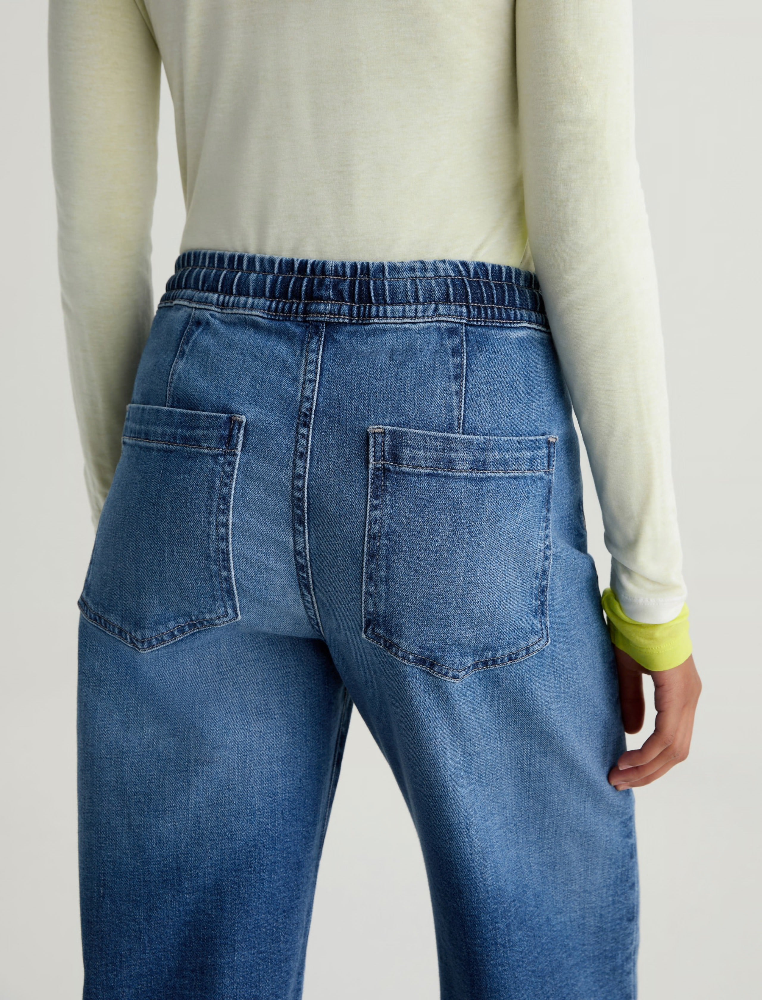 Person wearing blue jeans and a light-colored sweater on a plain background