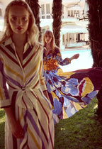 Two women in colorful SARA ROKA outfits standing by a poolside with palm trees in the background shop line