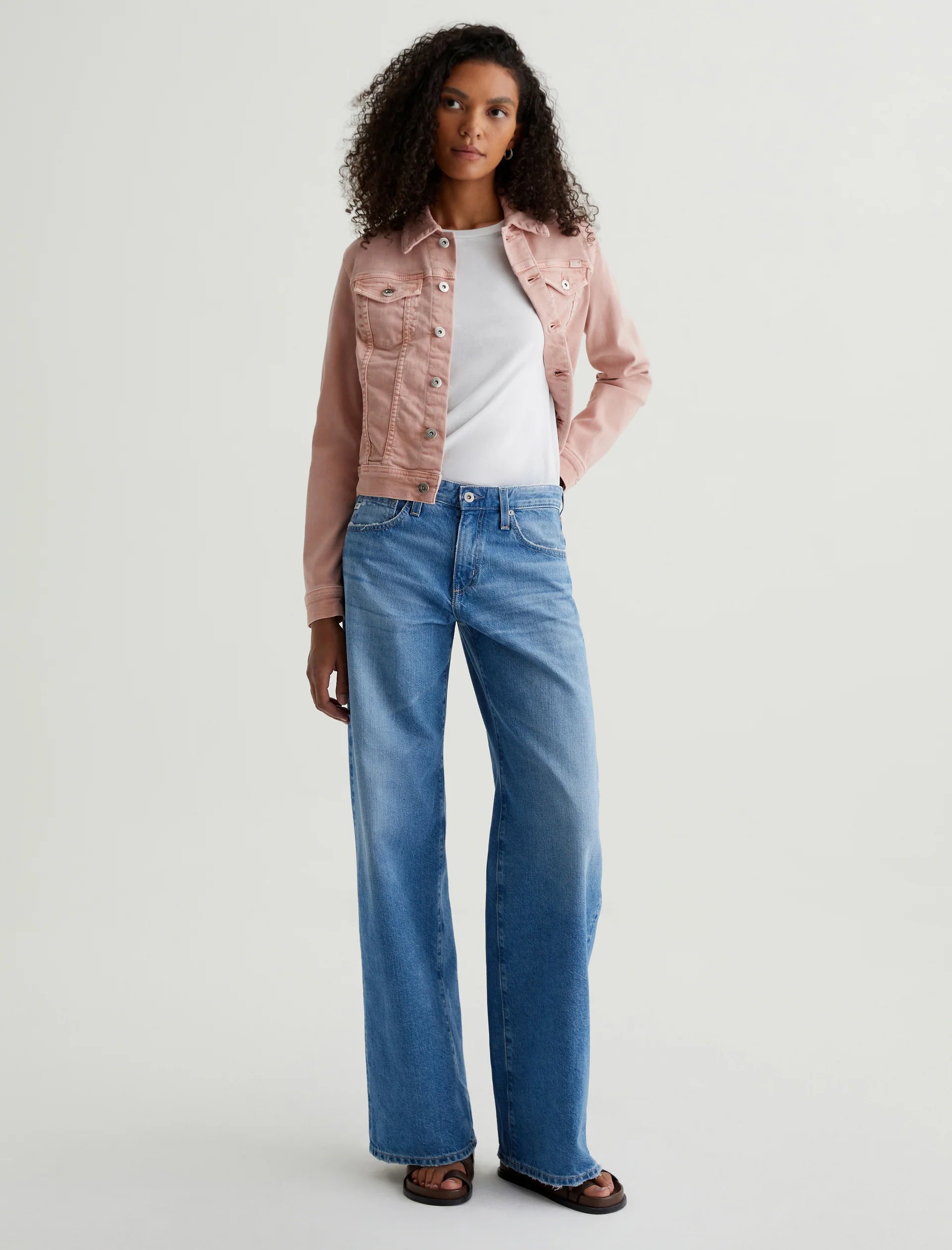 A female model wearing low-rise wide-leg jeans and a pink jacket with a white top.