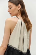 Woman wearing a beige sleeveless top with black trim on a white background