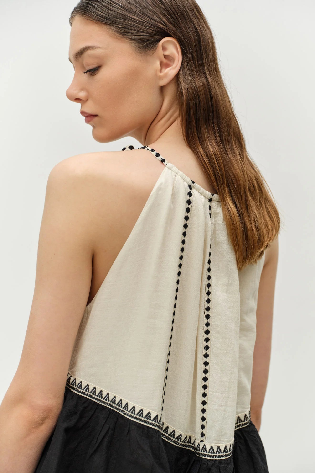 Woman wearing a beige sleeveless top with black trim on a white background