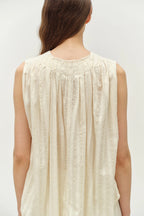 Woman wearing a beige sleeveless top against a white background