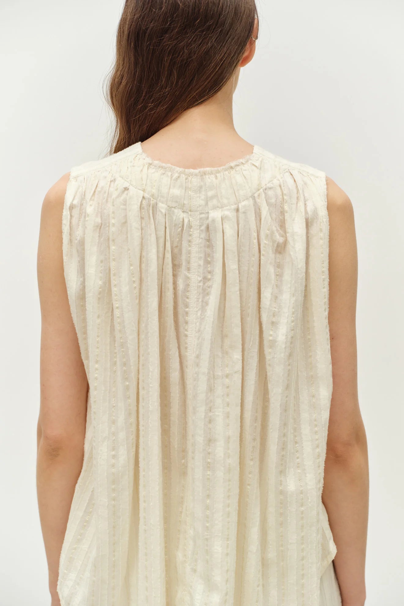 Woman wearing a beige sleeveless top against a white background