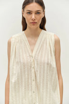 Woman wearing a light-colored sleeveless top against a plain background