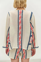 Person wearing a cream-colored top with red and blue striped patterns on a plain background