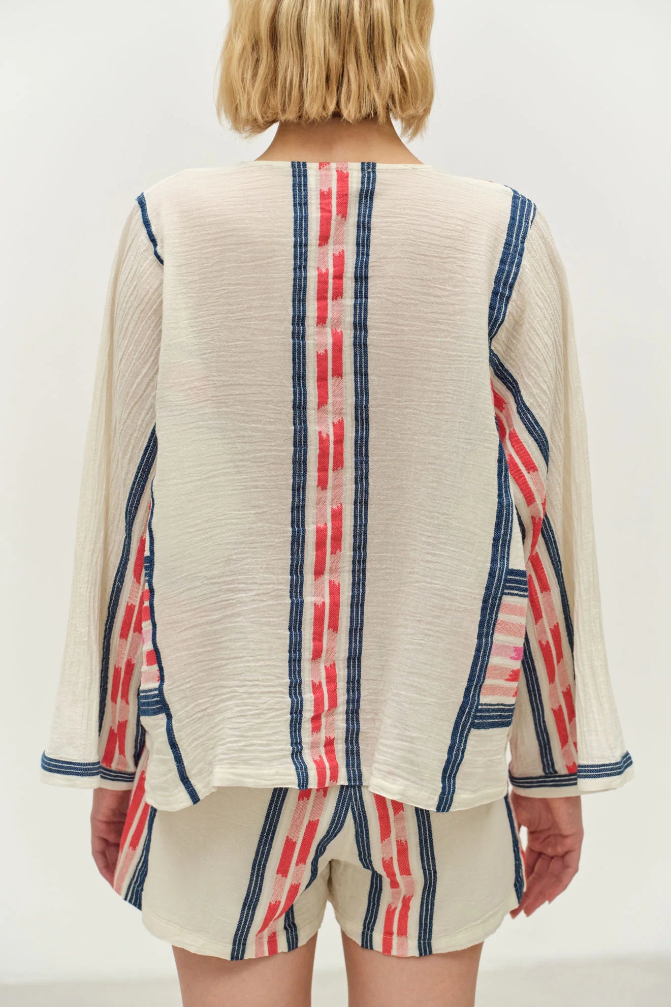 Person wearing a cream-colored top with red and blue striped patterns on a plain background