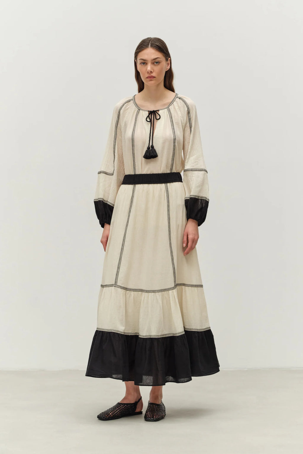 Woman wearing a long, cream-colored dress with black accents on a white background