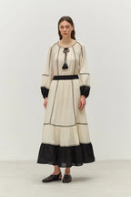 Woman wearing a long, cream-colored dress with black accents on a white background