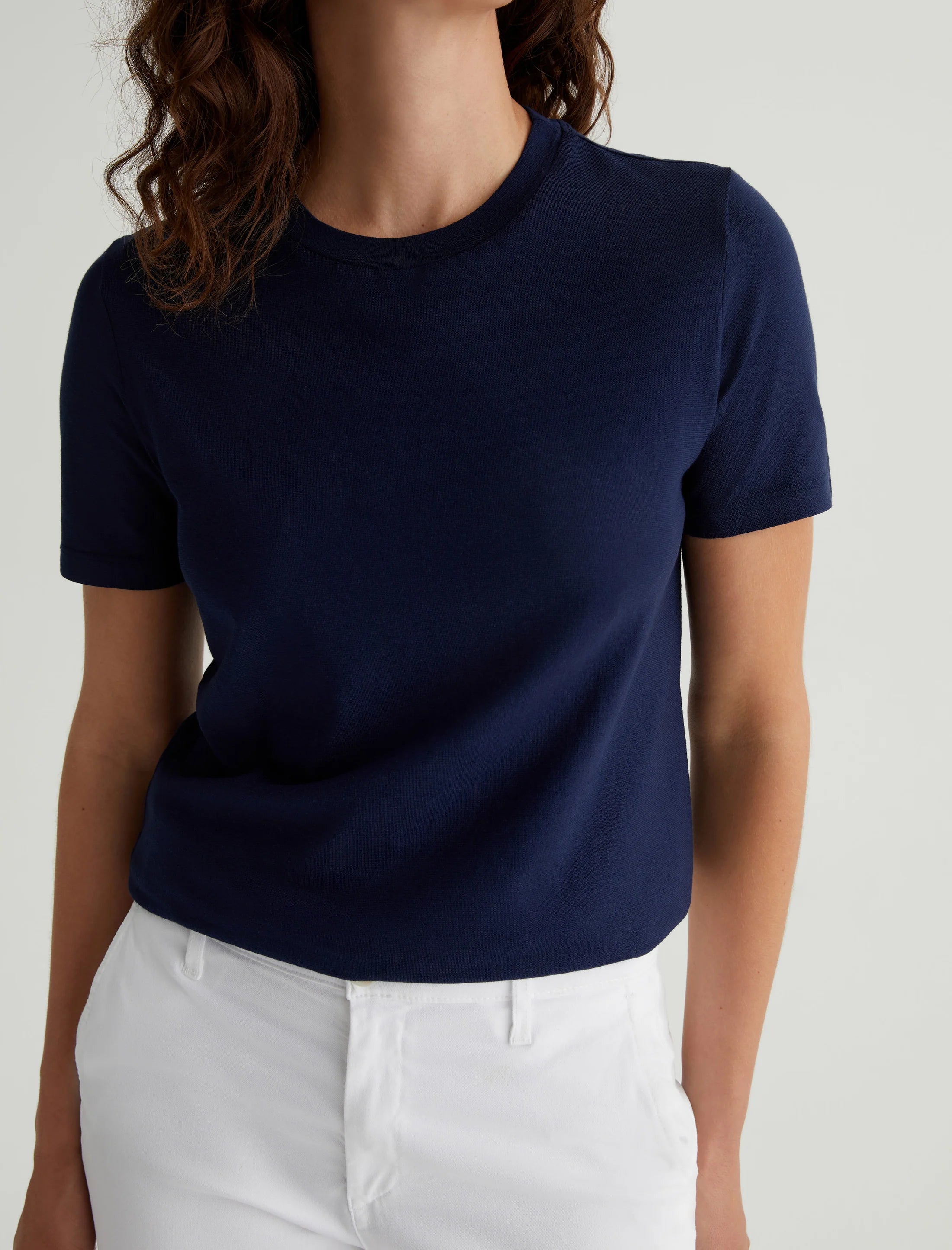 A woman wearing a navy blue crew neck t-shirt and white pants.