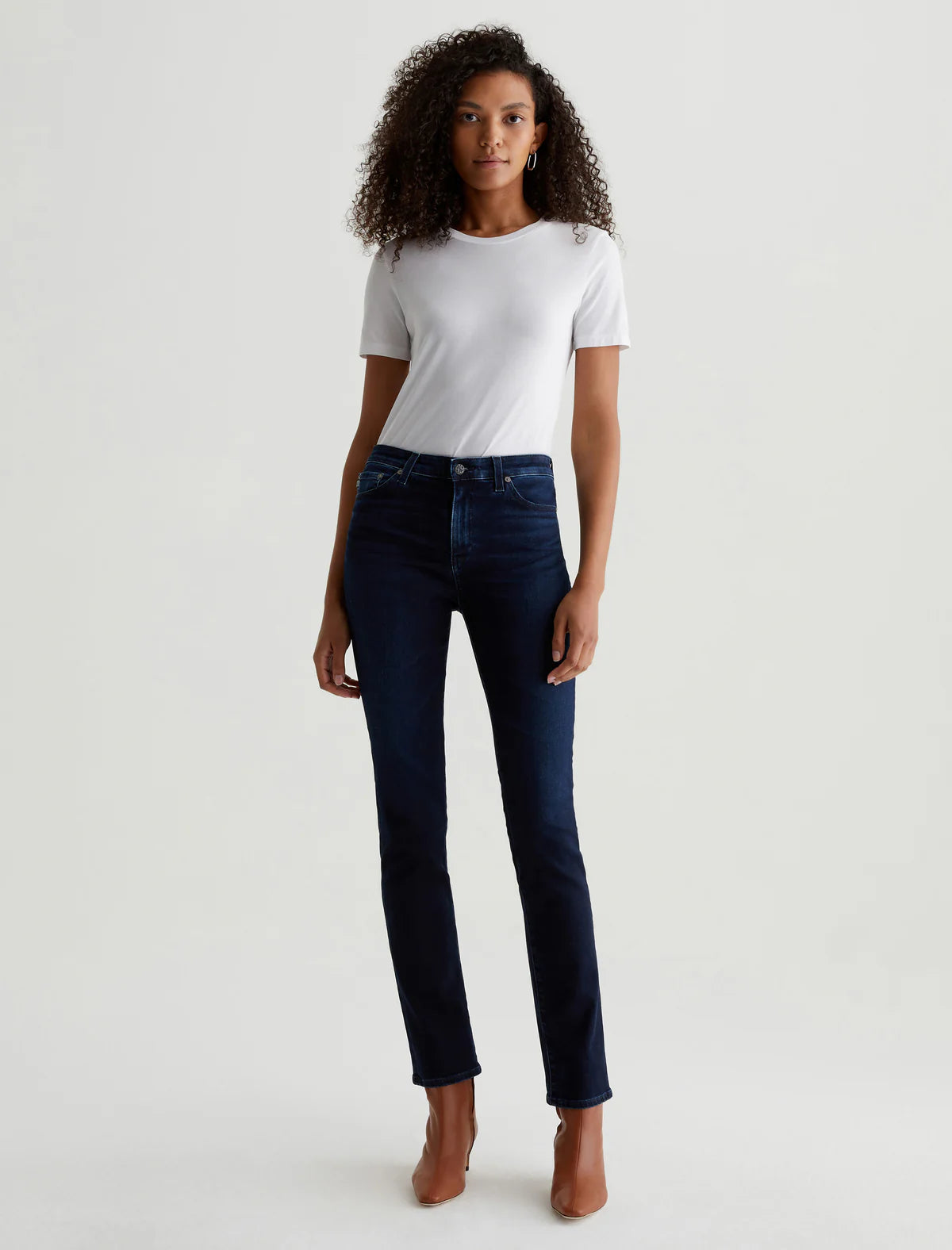 A person standing wearing mid-rise slim straight leg dark denim jeans and a white t-shirt.