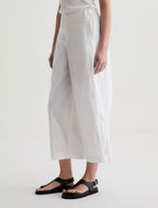 Person wearing white wide-leg pants and black sandals on a plain background