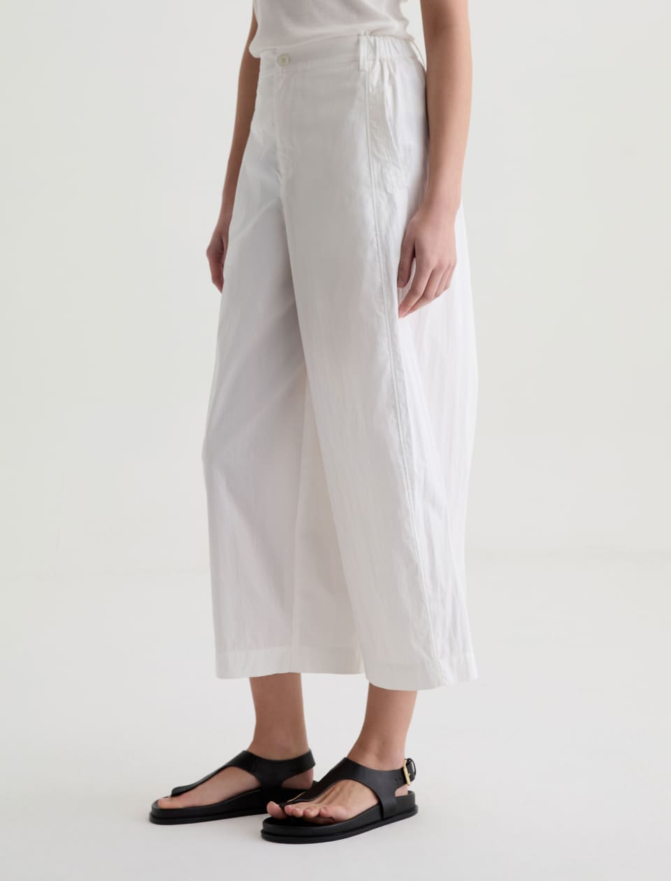 Person wearing white wide-leg pants and black sandals on a plain background
