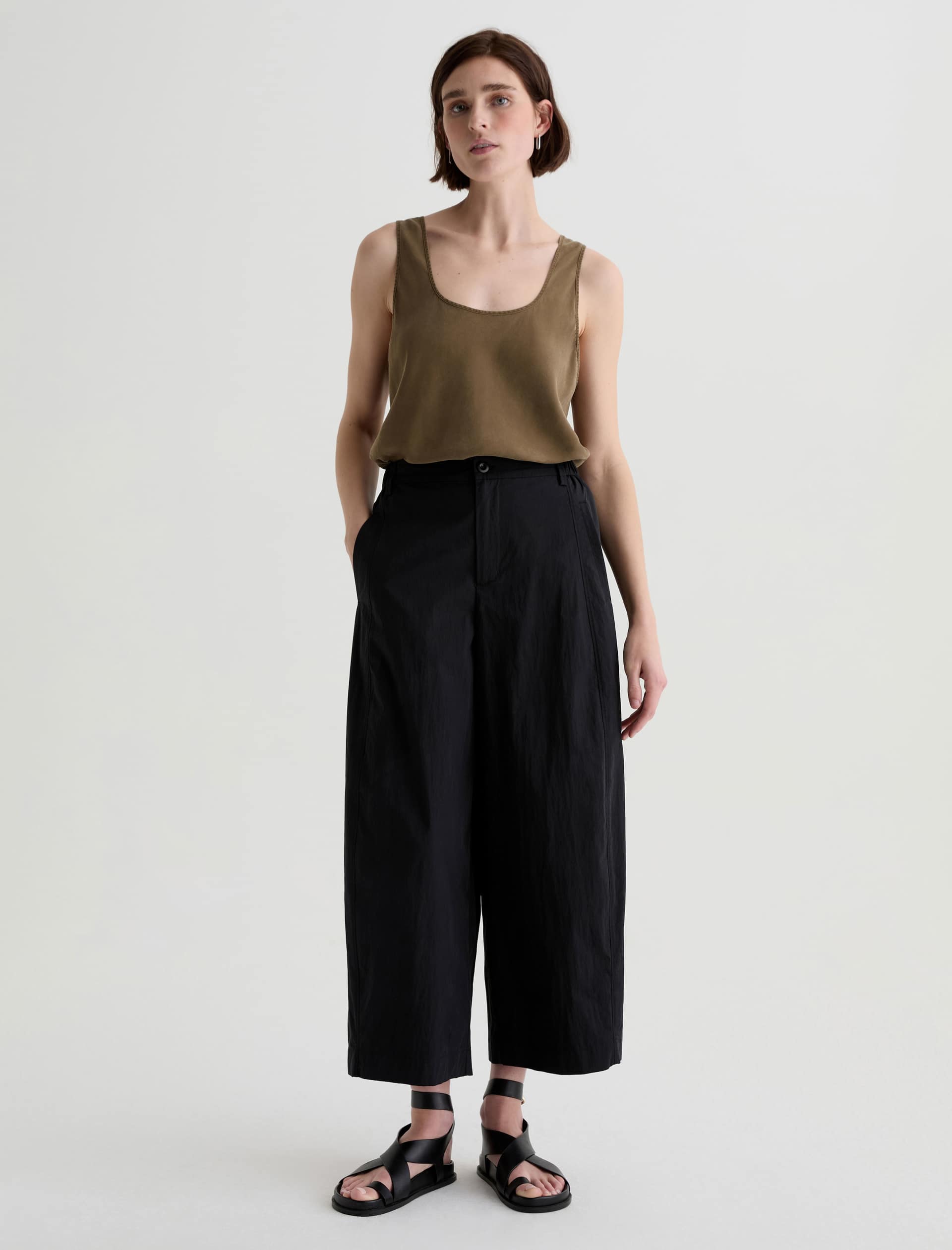 Woman wearing a green tank top and black wide-leg pants on a white background