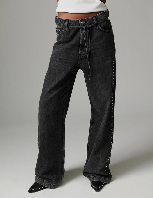 Black wide-leg jeans with studded details on a gray background