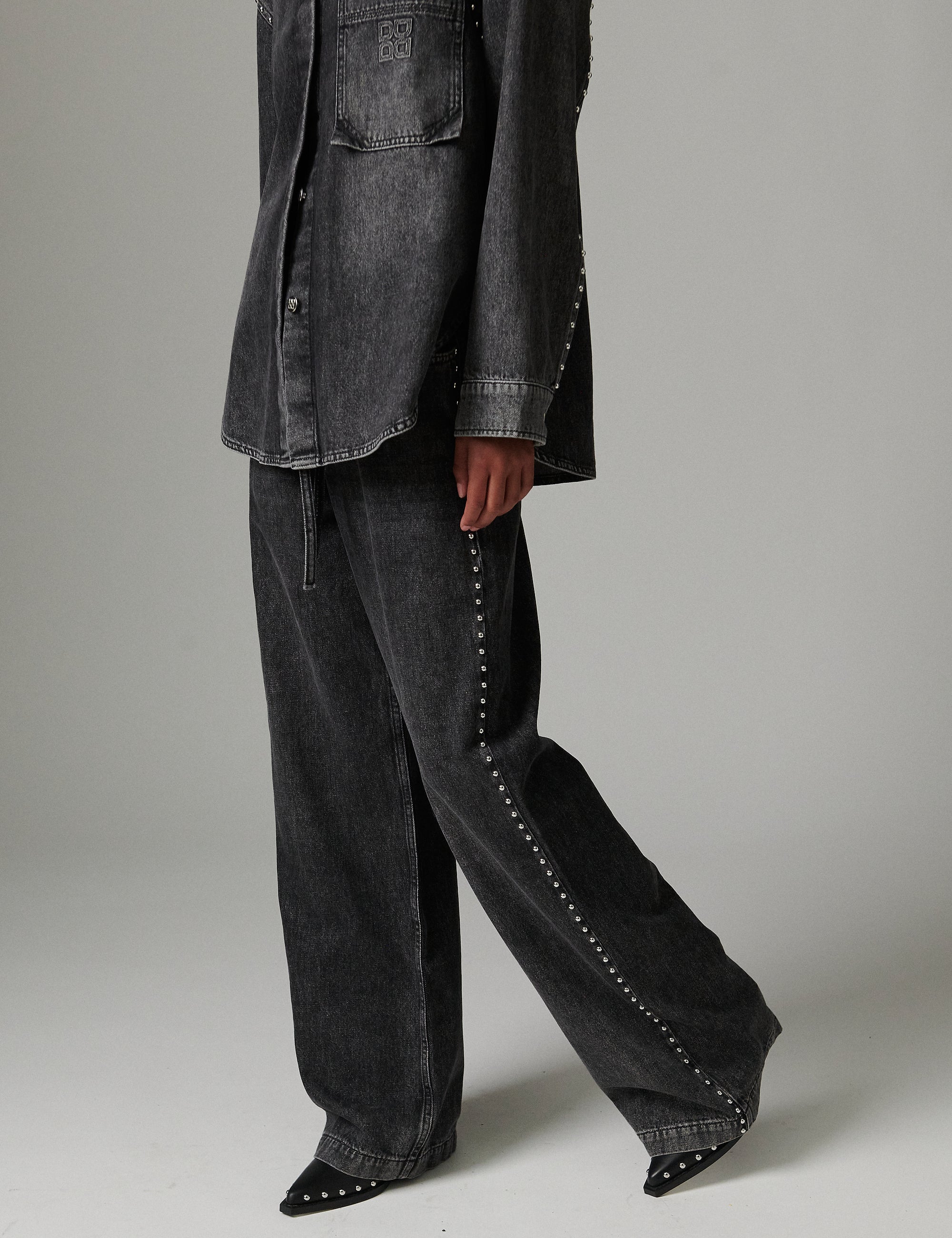 Person wearing a dark gray jacket and wide-leg pants on a plain background