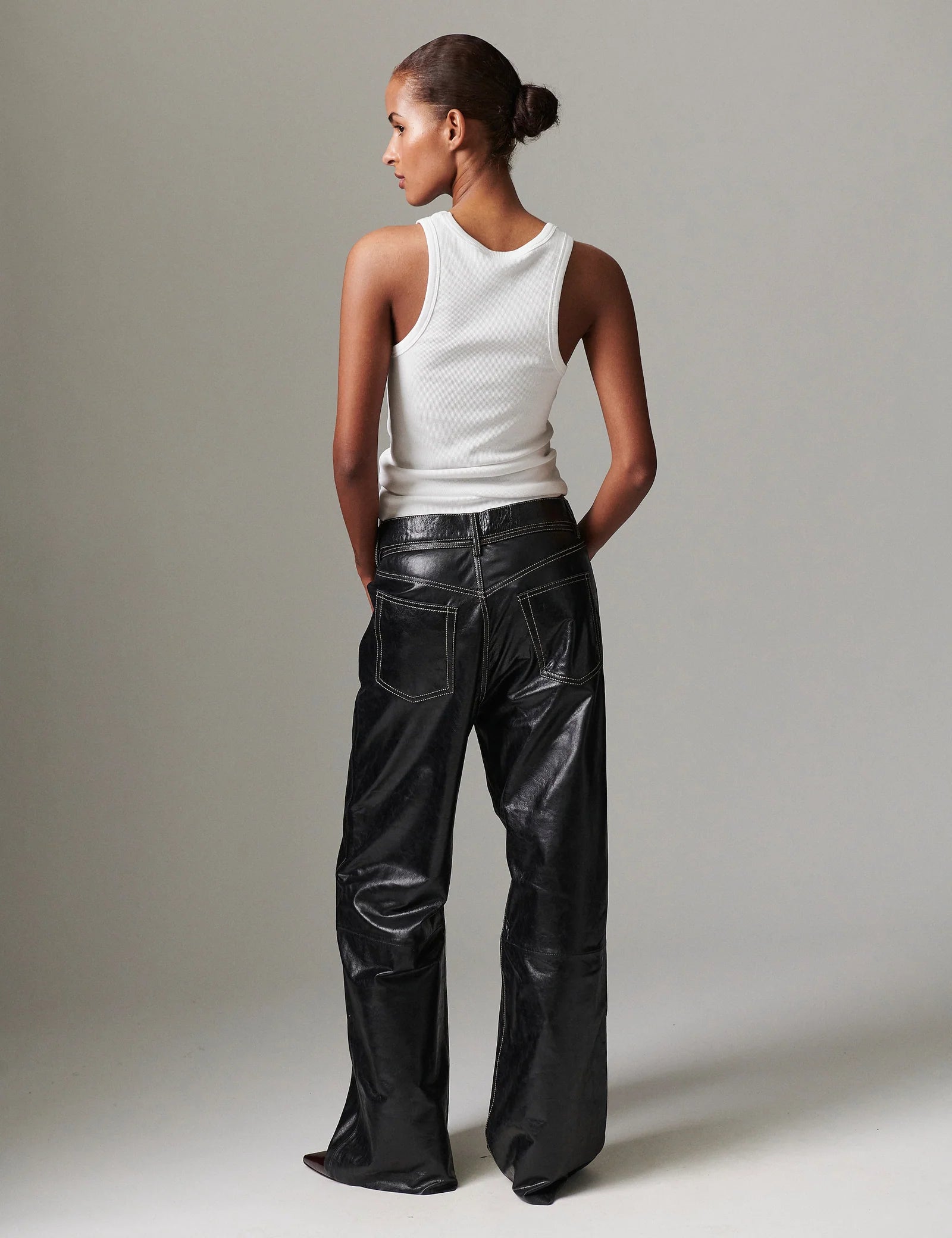 Person wearing a white sleeveless top and black leather pants against a neutral background