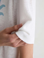Close-up of a person's hand pulling up the cuff of a white short-sleeve knit top, showing the fabric texture and hem stitching.