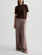 A model wearing a dark brown short-sleeve t-shirt and wide-leg taupe trousers, styled with a brown belt and flat sandals against a light gray studio background.