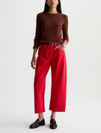 A model wearing a dark brown long-sleeve top, bright red cropped wide-leg pants, a black belt, and black leather loafers, standing against a plain white studio background.