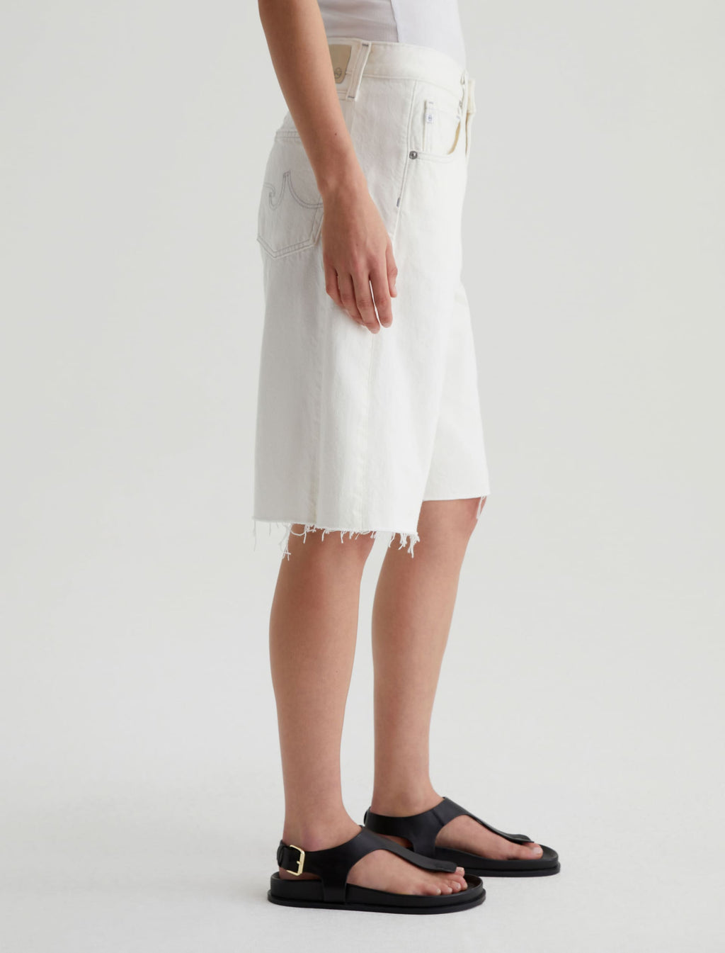 Person wearing a white denim skirt and black sandals on a plain background