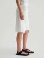 Person wearing a white denim skirt and black sandals on a plain background
