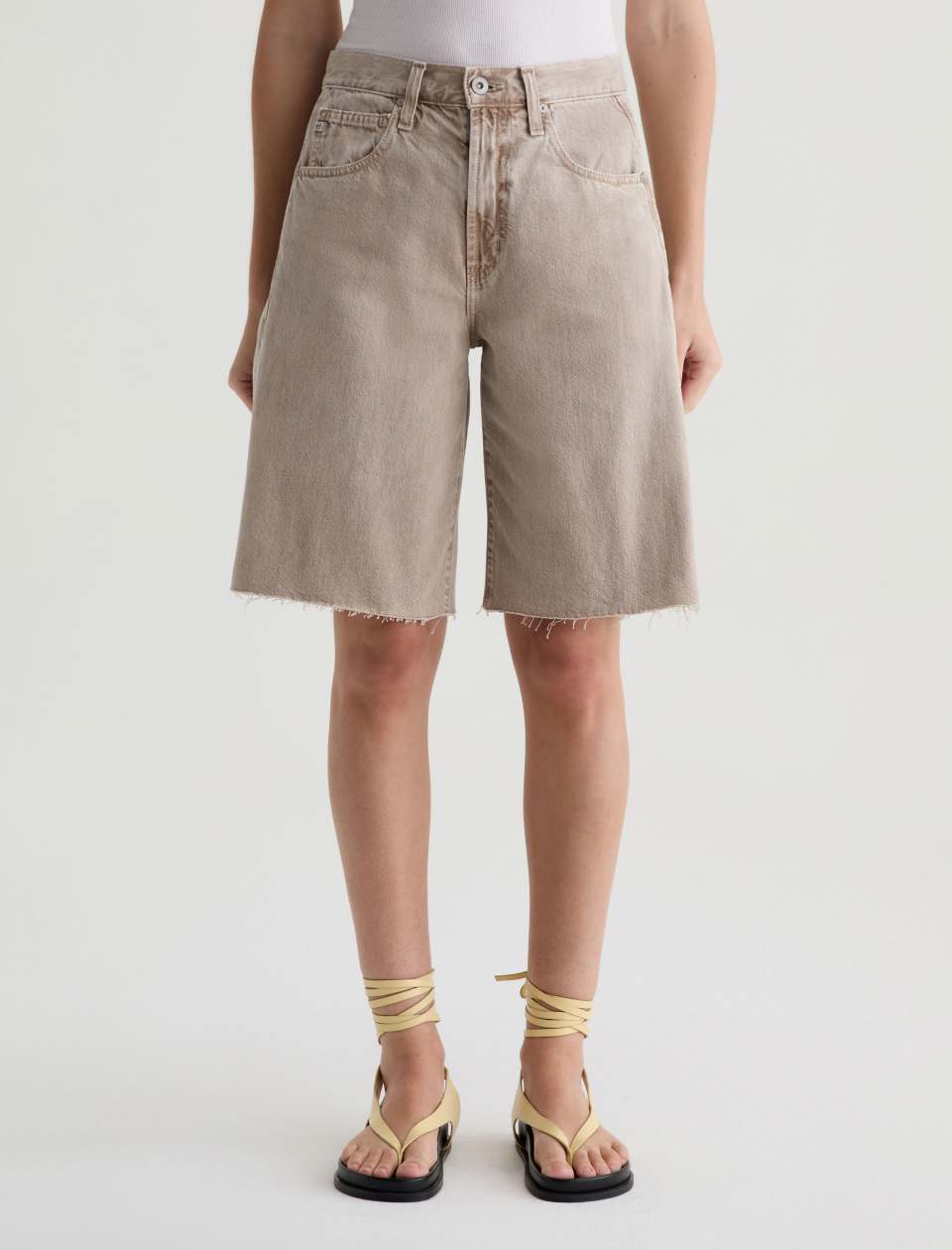 Person wearing beige denim shorts on a white background