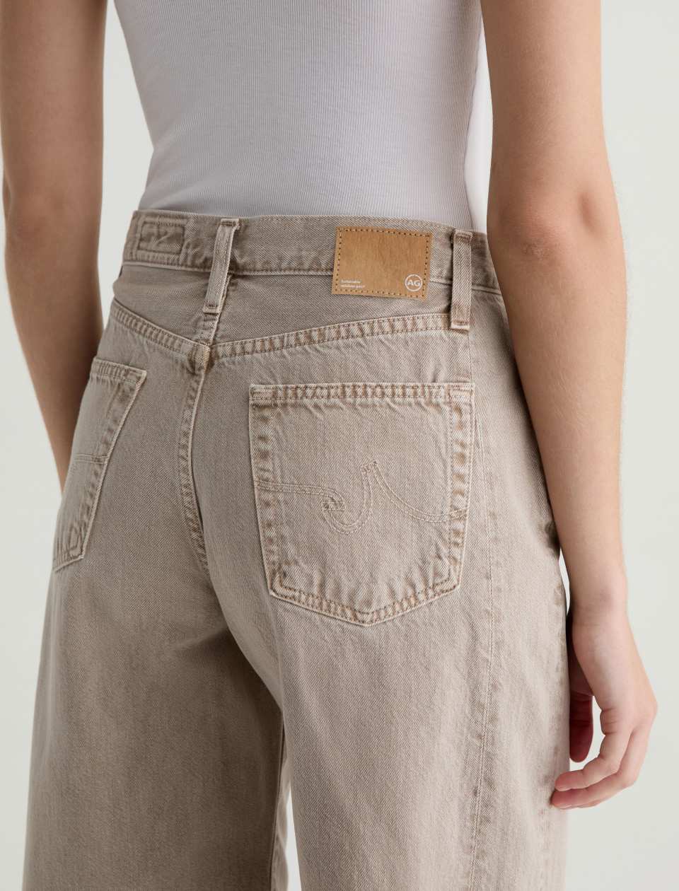 Person wearing beige jeans with a visible brand logo on a plain background