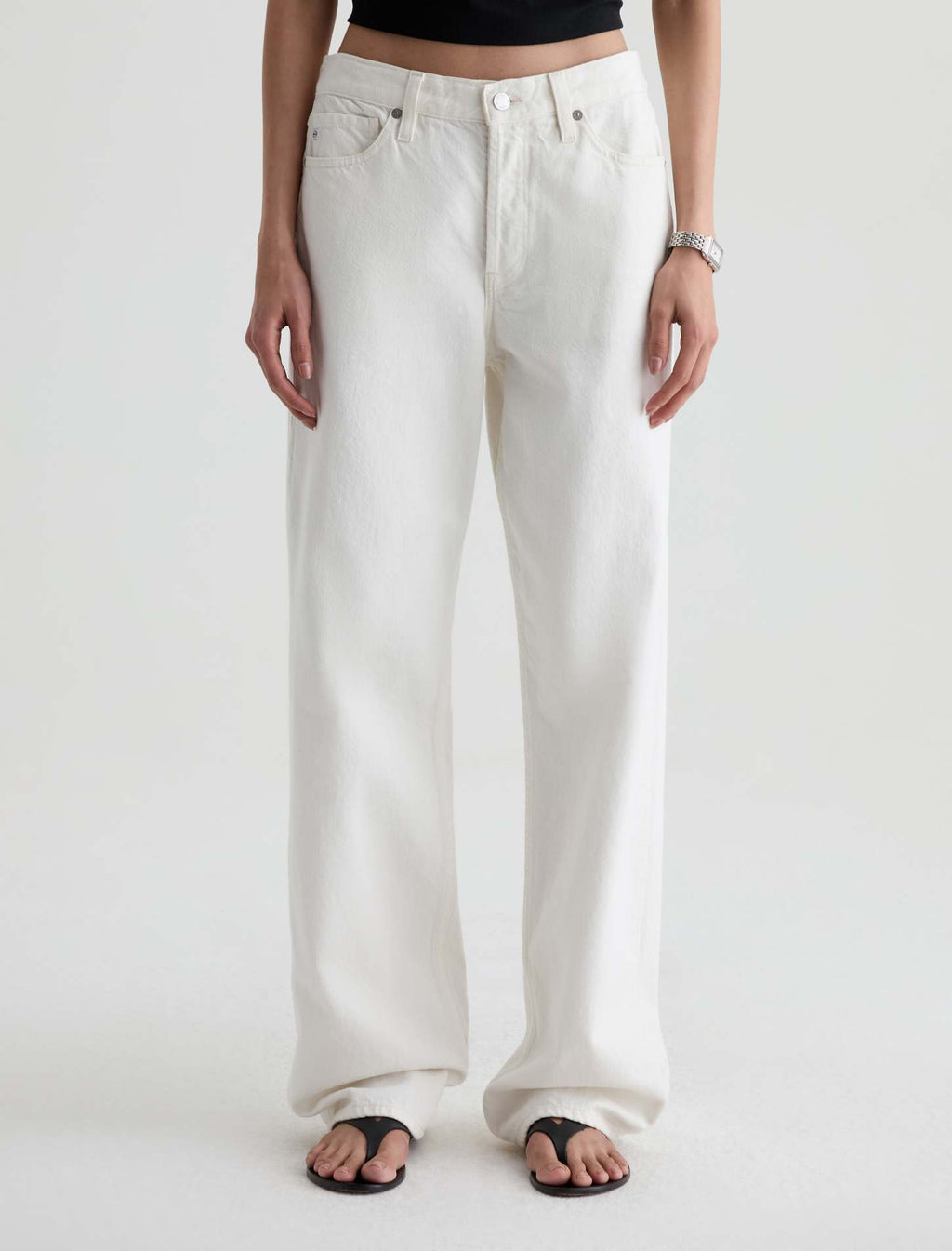 A person wearing off-white wide-leg jeans with a black crop top and black flip-flop sandals, shown from the waist down against a plain light background.