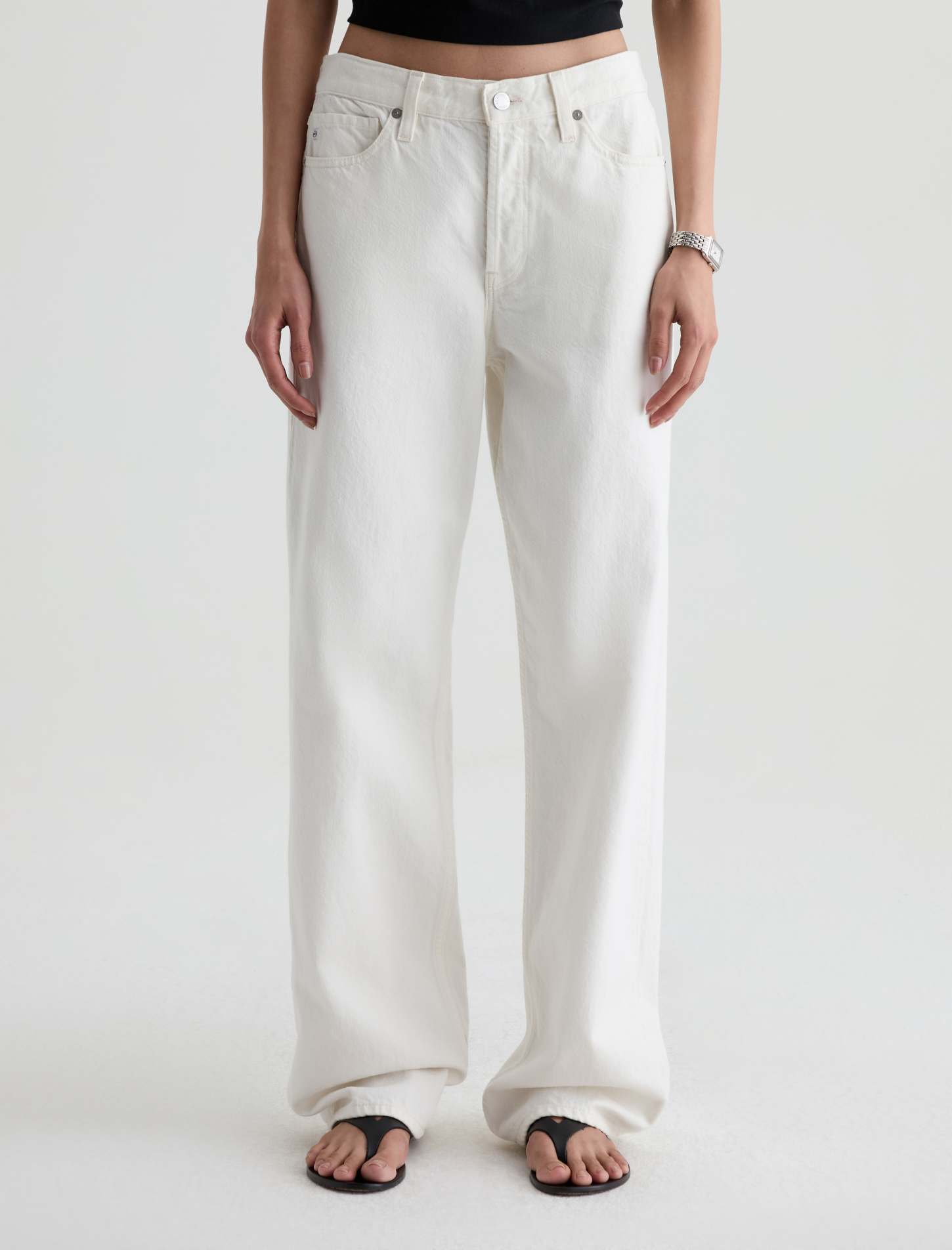 A person wearing off-white wide-leg jeans with a black crop top and black flip-flop sandals, shown from the waist down against a plain light background.