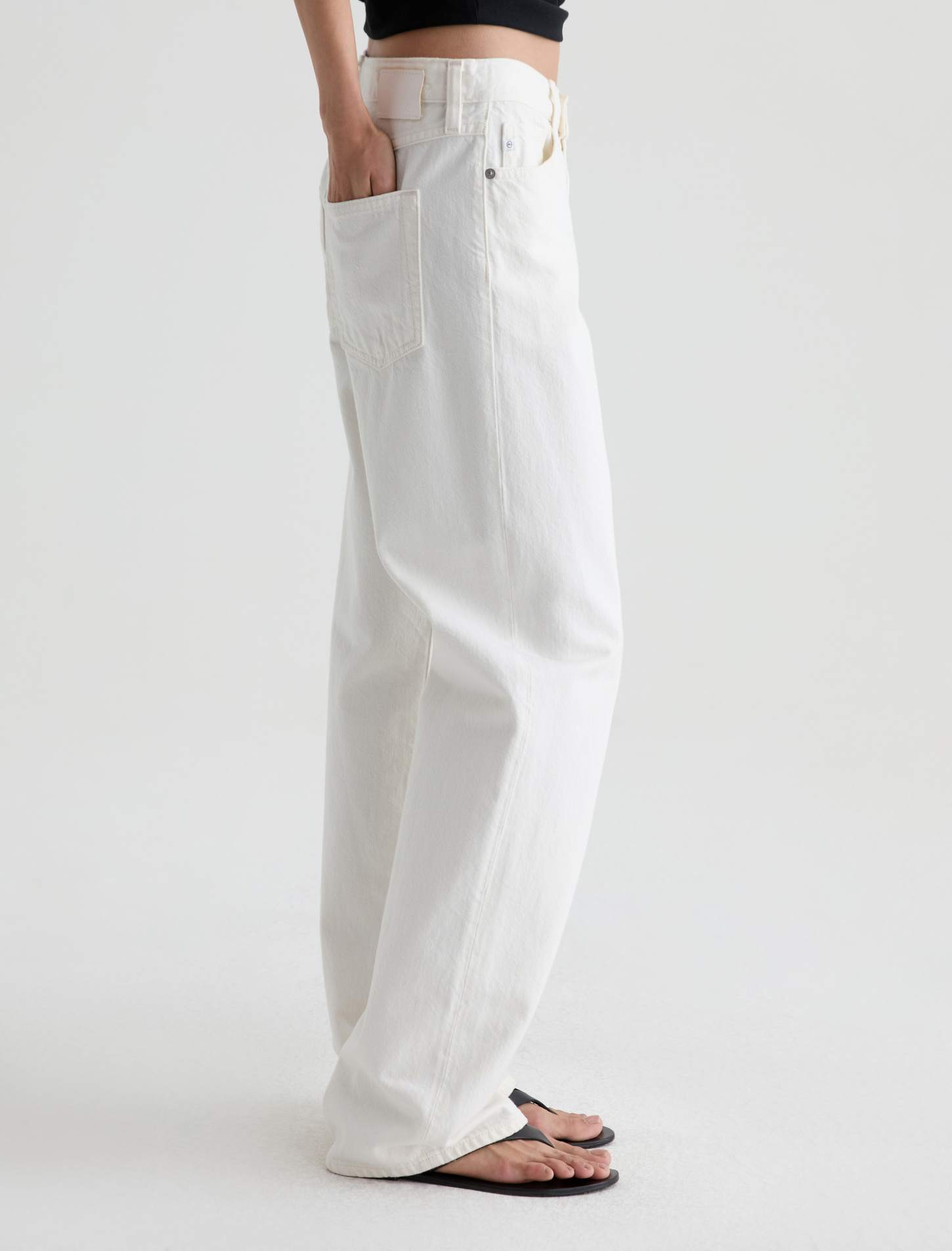 White wide-leg denim jeans shown on a model from the waist down, paired with black flip-flops against a clean white studio background.