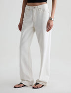 A model wearing a pair of off-white, wide-leg denim jeans with a black crop top and black flip-flops, shown from the waist down against a light gray studio background.