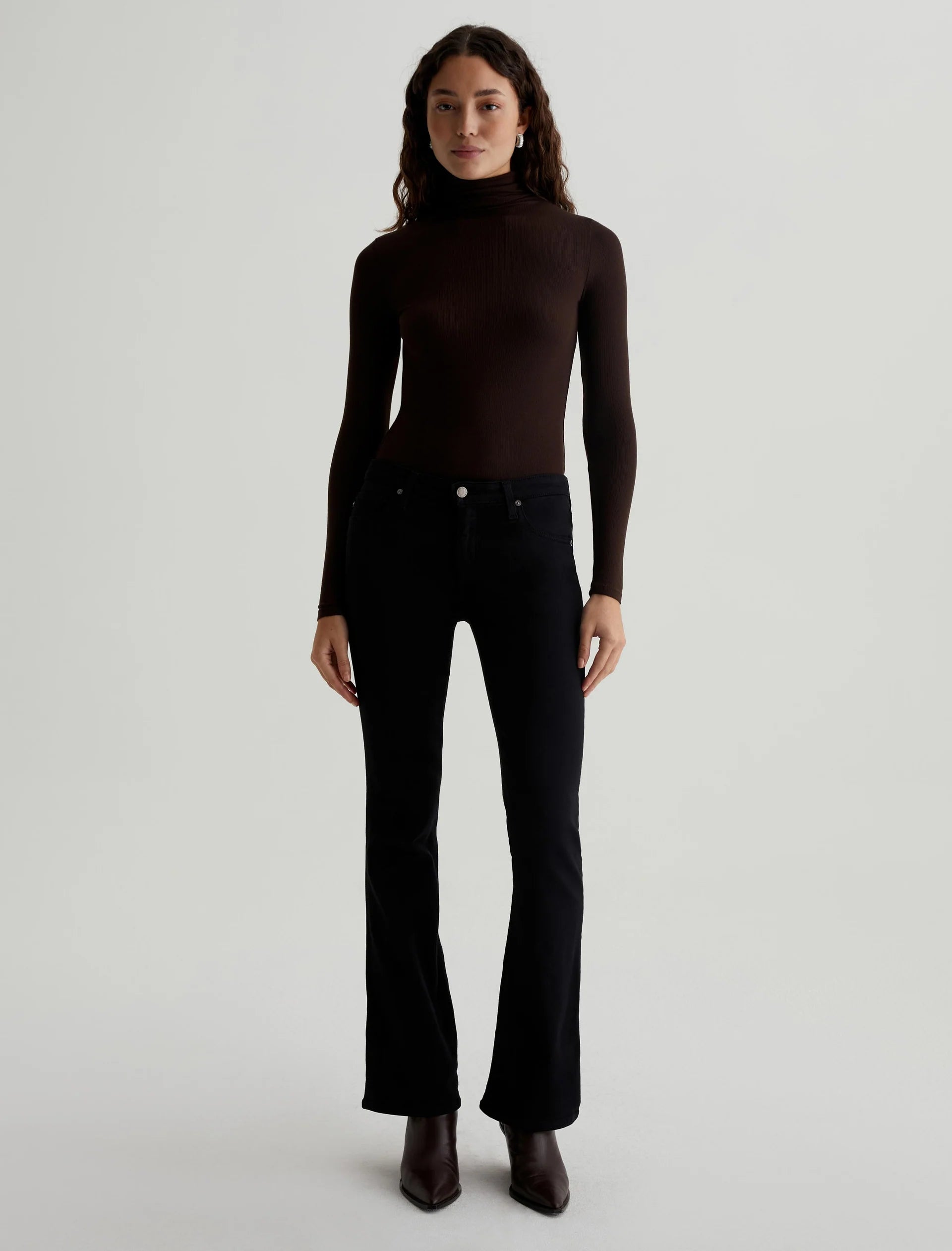 A person standing wearing a low-rise black bootcut pair of jeans and a brown turtleneck top.