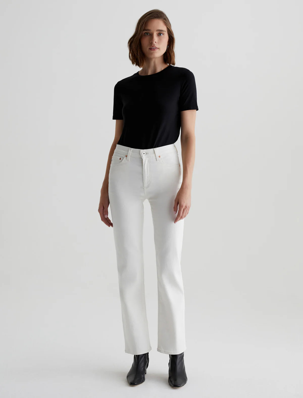 A woman standing straight facing forward, wearing a black t-shirt and mid-rise straight white jeans with visible five pockets, paired with black ankle boots.