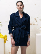 Woman wearing a navy blue trench coat over a patterned dress against a white background with floral decorations.