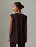 Woman wearing a brown sleeveless top against a gray background