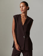 Woman wearing a brown sleeveless top with a button detail against a gray background