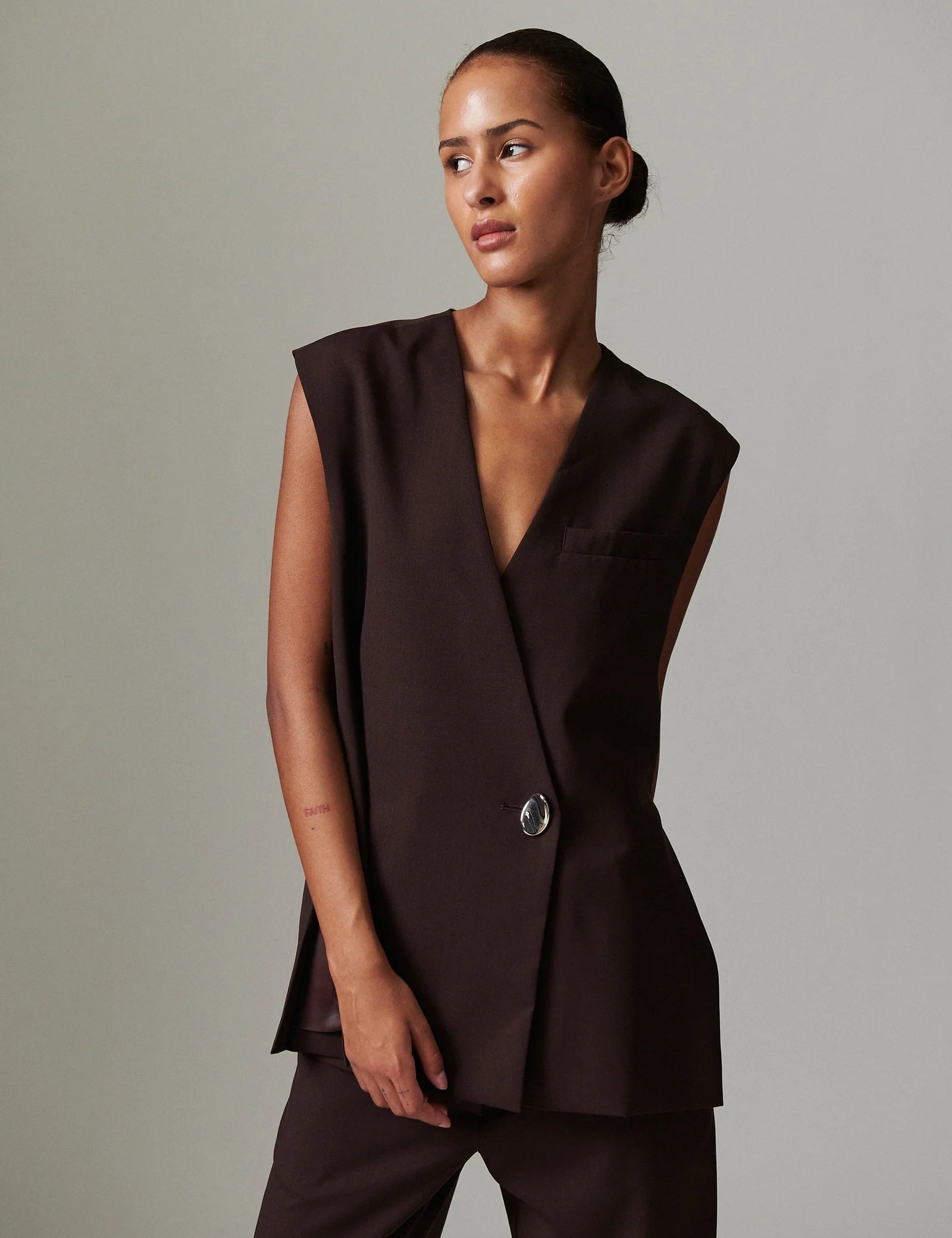 Woman wearing a brown sleeveless top with a button detail against a gray background