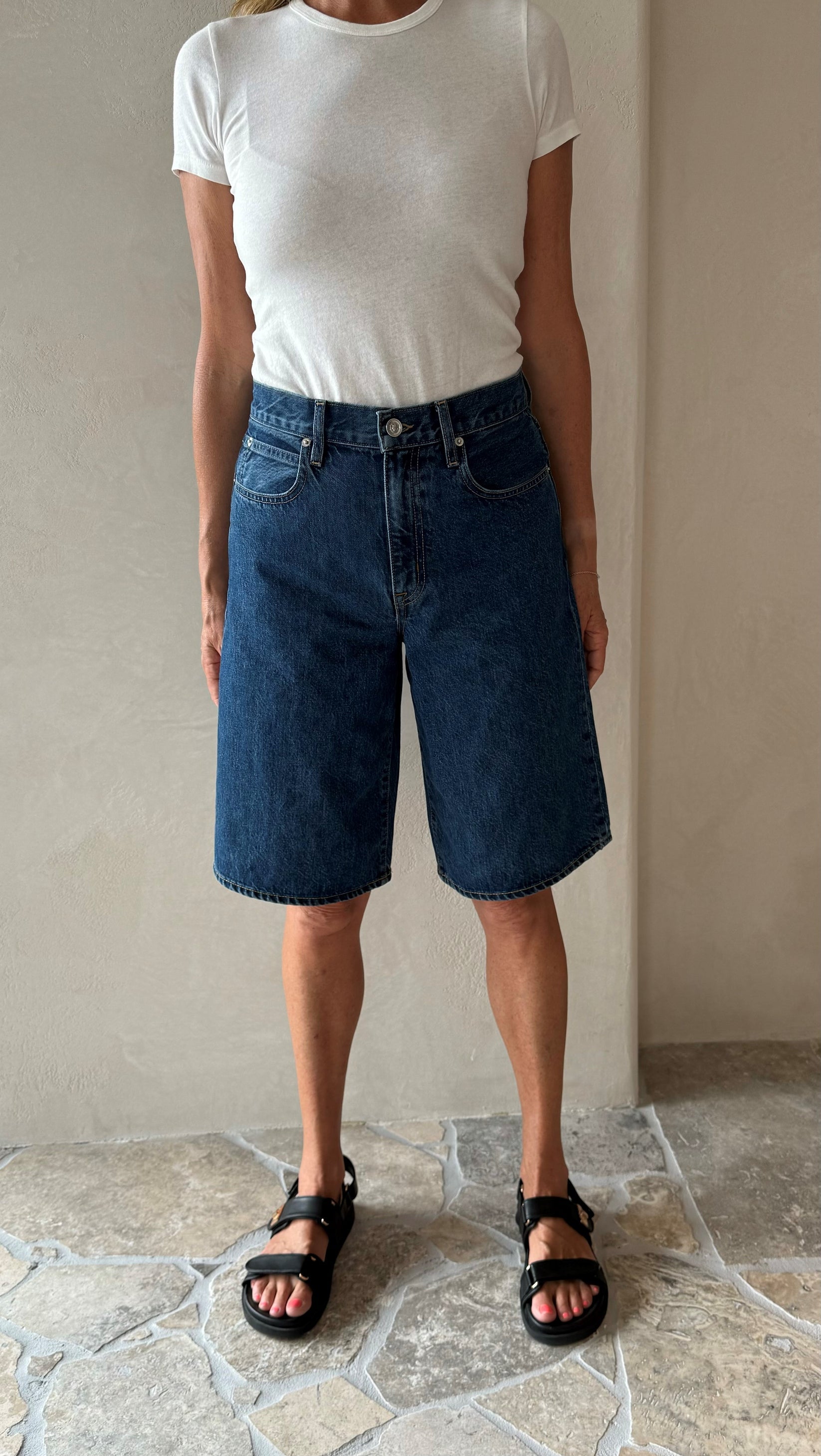A pair of blue denim shorts with a button-up front, worn by a person standing indoors.