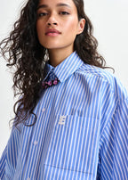 Person wearing a blue and white striped shirt with a brand logo on a plain background