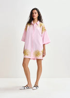 Woman wearing a pink dress with gold floral patterns on a white background