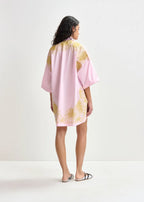 Woman wearing a pink kimono-style garment with gold patterns on a white background