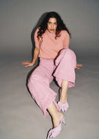 A woman sitting wearing a short-sleeve jacquard knit top in a mauve color with ribbed trims and contrasting orange dots, paired with matching wide-leg pants and orange shoes.