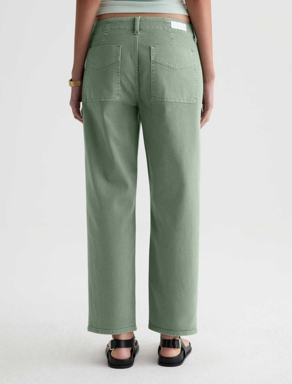 A person shown from the back wearing sage green wide-leg cropped pants, a light mint top, and black sandals against a plain light gray studio background.