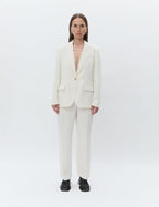 A person standing against a white background, wearing an ivory  day birger et Mikkelsen colored blazer with a single button closure and patch pockets, paired with matching trousers.