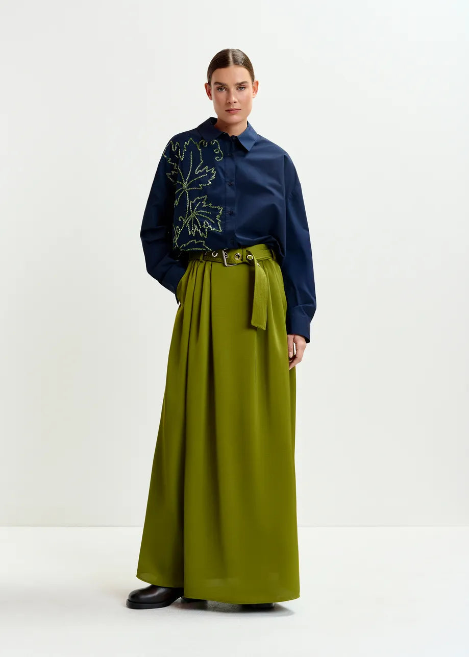 Woman wearing a navy shirt with leaf pattern and a long green skirt on a white background