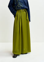 Person wearing a navy blue top with floral embroidery and a green wide-leg pants on a white background