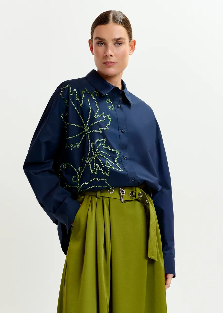 Woman wearing a navy blue shirt with green embroidery and green pants on a white background