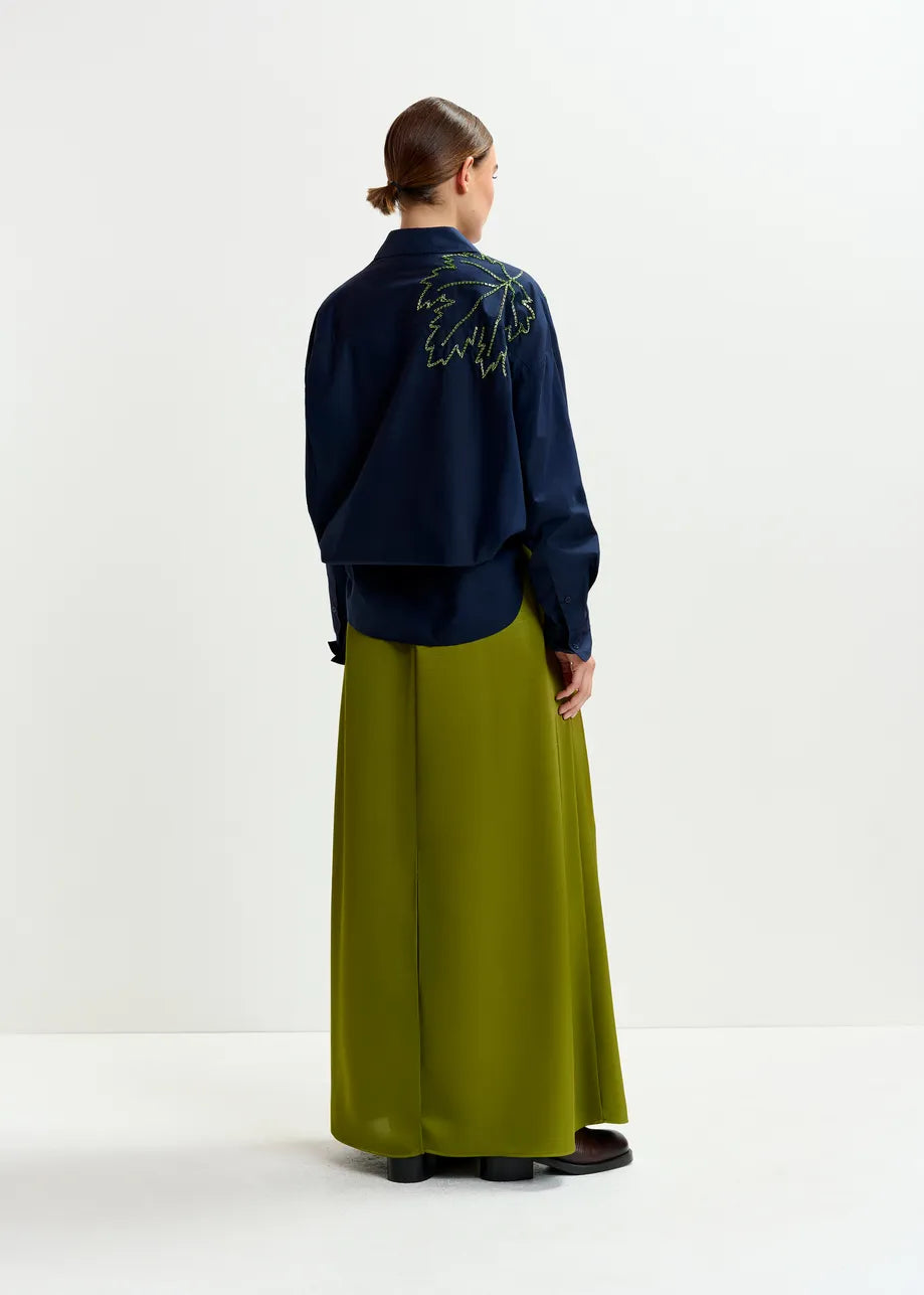 Person wearing a navy jacket with embroidery and green pants on a white background