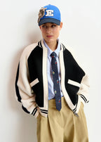 Person wearing a varsity jacket, tie, and cap against a white background