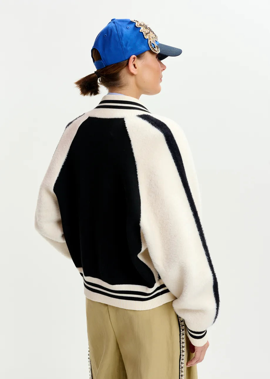 Person wearing a black and white varsity jacket with beige pants on a light gray background